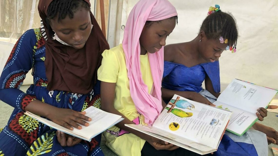 Trois collegiennes plongees dans des romans et livres pour ados lors des 72 heures du livre a Conakry